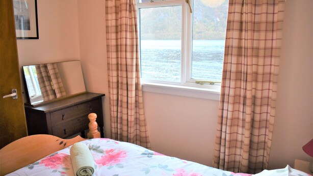 A bedroom with a bed, a dresser, a mirror, and a window with curtains. - Camus Slatach - sleeps 4 guests  in 2 bedrooms (Glenfinnan)