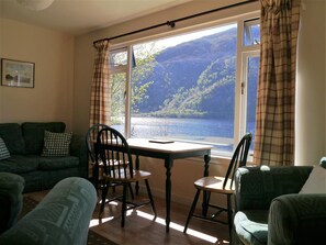 Une pièce confortable avec vue sur un lac et des montagnes, aménagée avec un canapé, des fauteuils et une table.