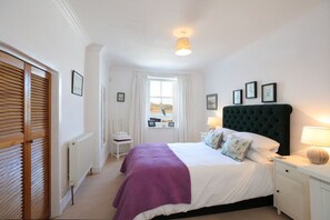 A bedroom with a bed, bedside lamps, a window with curtains, and framed pictures on the wall.