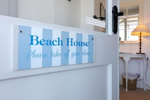 A sign on a door that reads "Beach House Please take off your shoes."