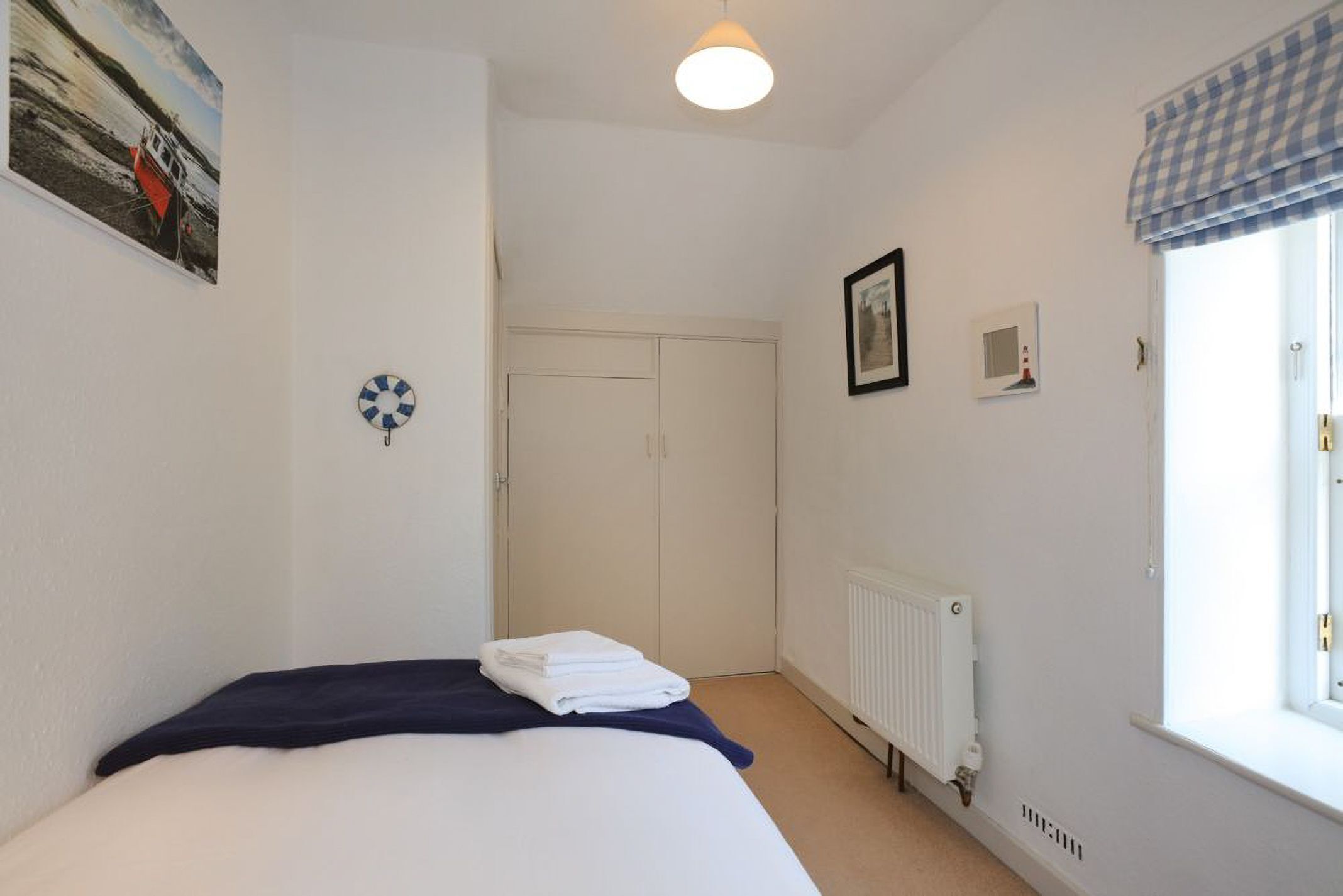 A bedroom with a bed, a radiator, a window with a checkered valance, and a door.
