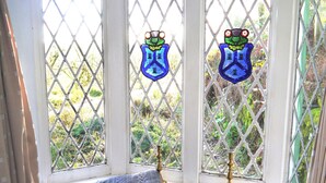 Un ventanal con vidrieras de colores, un banco acolchado y un candelabro de latón.