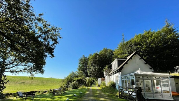 Propiedad rural con una casa blanca, un espacio de estar techado al aire libre y un césped.
