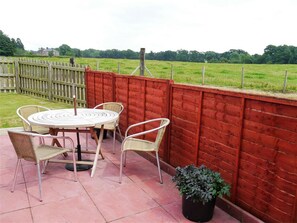 Une terrasse extérieure avec une table ronde et quatre chaises, une clôture rouge et un pot de fleurs.