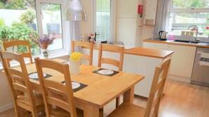 A dining area with a wooden table and chairs, a vase with flowers, and a window with a view of greenery. - Arakhova -  a house that sleeps 10 guests  in 4 bedrooms (Kirkcudbright)