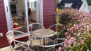 An outdoor patio with a table and chairs, a glass door leading inside, and a garden with pink flowers. - Arakhova -  a house that sleeps 10 guests  in 4 bedrooms (Kirkcudbright)