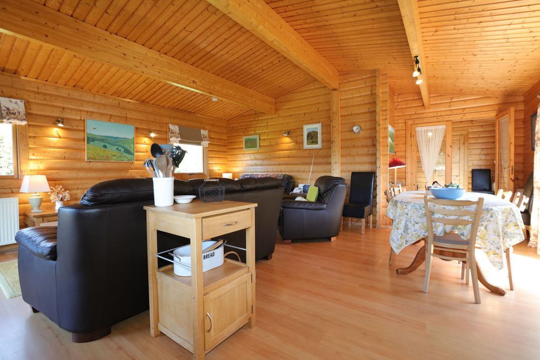 A wooden cabin interior with a living area, a dining table, and a kitchen counter.
