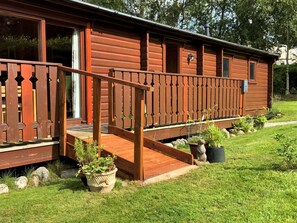 A wooden cabin with a porch, a staircase, and potted plants. - Birchlea - a lodge that sleeps 6 guests in 3 bedrooms (Kippford, Dalbeattie)