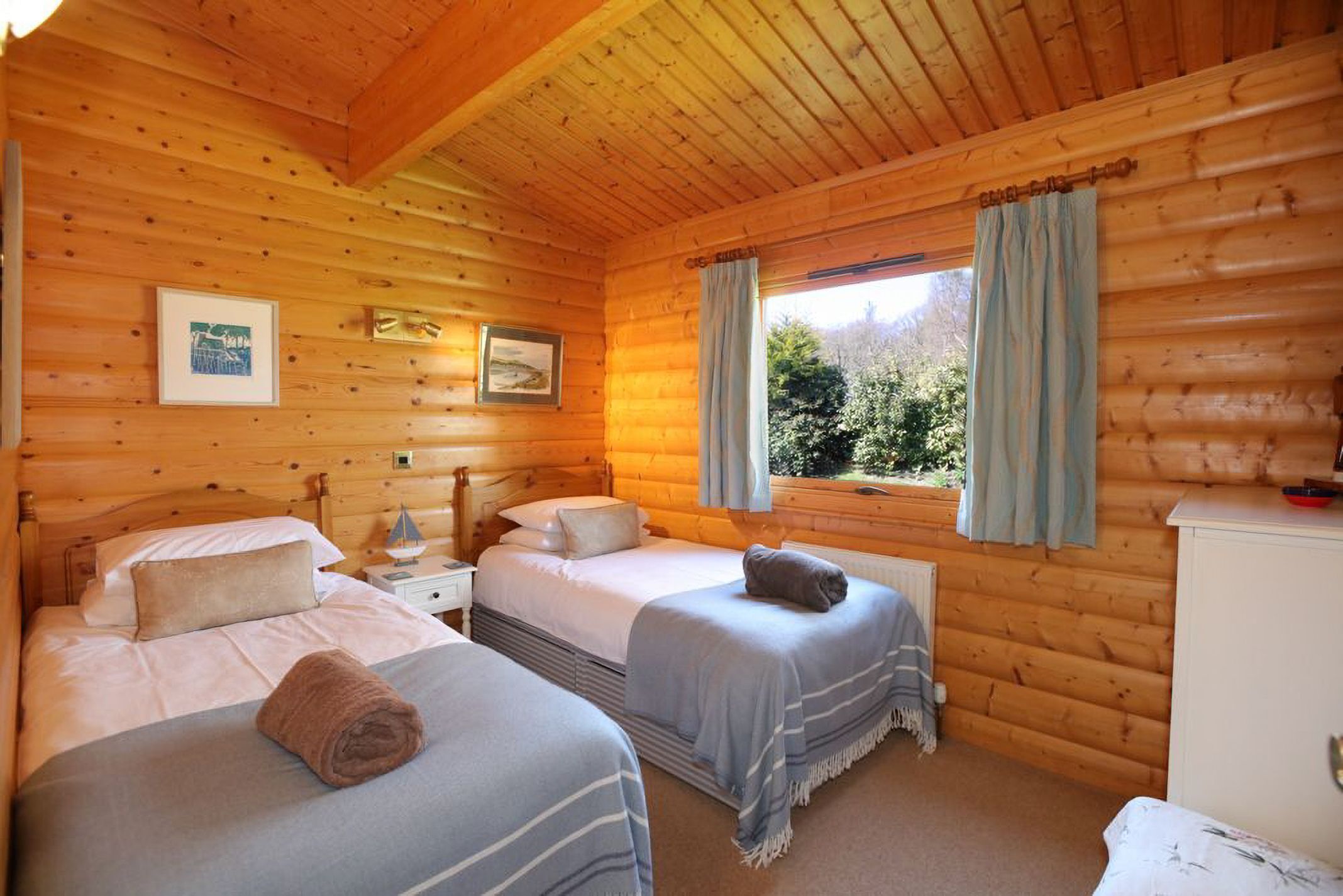 Een chalet met twee bedden, een nachtkastje, een raam met gordijnen en houten wanden.