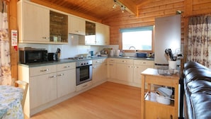 A compact kitchen with wooden cabinets, a microwave, a stove, and a sink. - Birchlea -  a lodge that sleeps 6 guests  in 3 bedrooms (Kippford, Dalbeattie)
