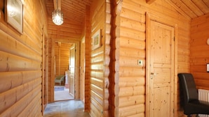 A wooden interior with a hallway leading to a door, a radiator, and a chair. - Birchlea -  a lodge that sleeps 6 guests  in 3 bedrooms (Kippford, Dalbeattie)