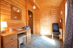 L’intérieur d’une cabane en bois, avec un bureau, une chaise et une porte donnant sur une autre pièce.