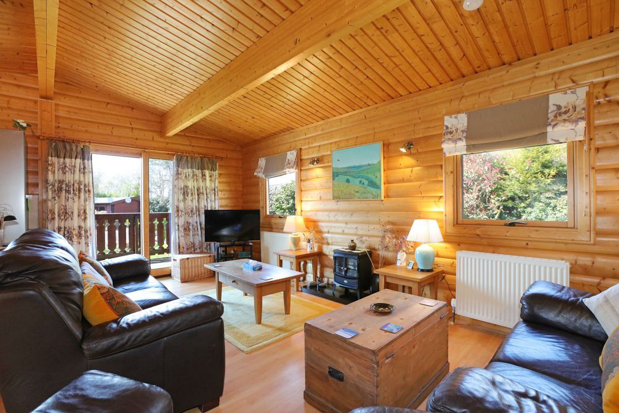 A wooden cabin interior with a sofa, television, table, and a fireplace.