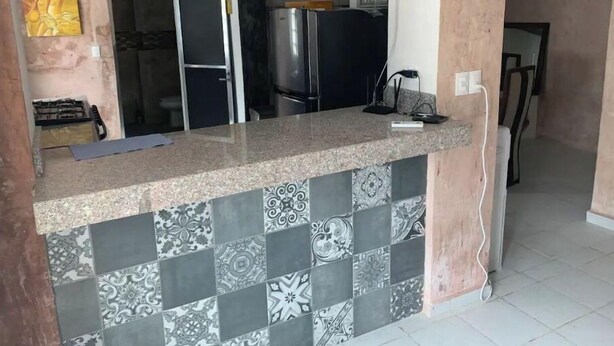 A kitchen with a granite countertop, patterned tiles, a ceiling fan, and a refrigerator. - Apartment Trankilo 1 (Progreso)