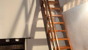 A bedroom with a wooden ladder leading to a loft, a red bedspread, a small table with a lamp, and a wall-mounted shelf. - Casa Miky (Palermo)