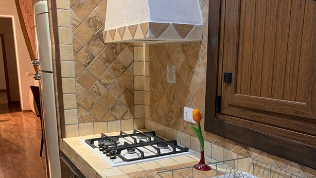 A kitchen with a gas stove, a white range hood, and a tiled backsplash. - Casa Miky (Palermo)
