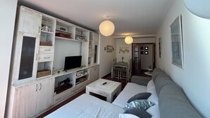 A compact living space with a sofa, a television, a cabinet with drawers, and a dining area with a table and chairs.