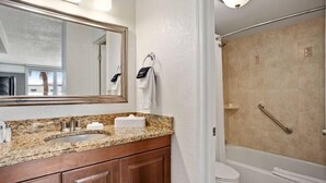Une salle de bain dotée d’un comptoir en granit, d’un lavabo, d’un miroir, d’un porte-serviettes et d’un espace douche équipé d’une barre d’appui.