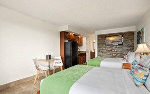 A hotel room with two beds, a kitchenette, a dining area, and a TV mounted on a stone wall. - Modern Suite Close to Medieval Times and Capone's Dinner Show (Kissimmee)
