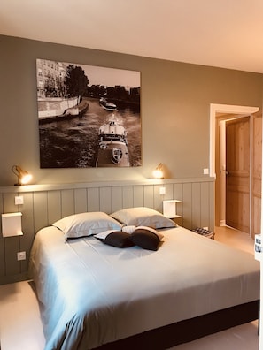 Quarto com cama, duas luminárias de cabeceira, um quadro na parede e uma porta de madeira.
