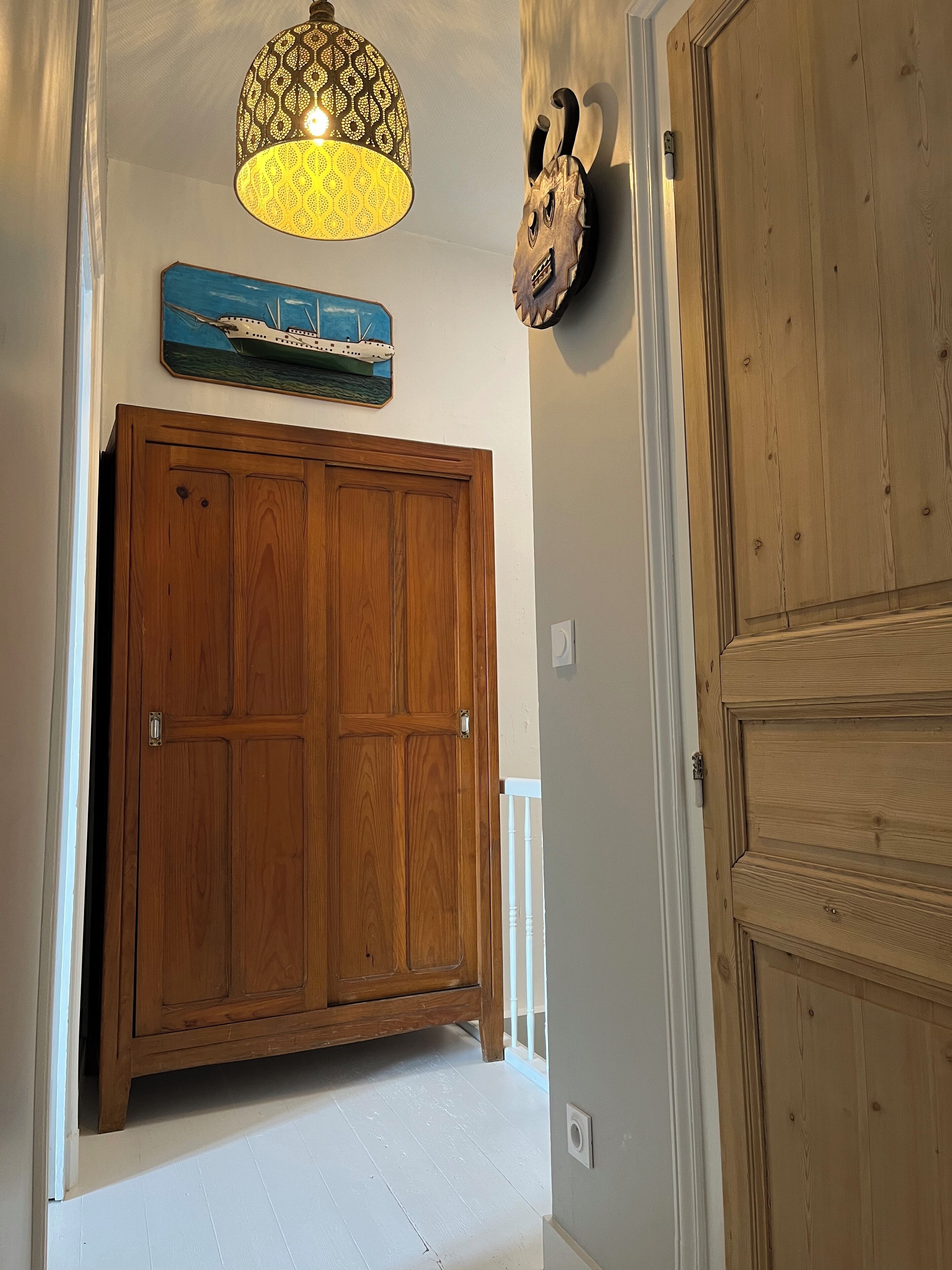 A hallway with a wooden wardrobe, a decorative wall hanging, and a patterned light fixture.
