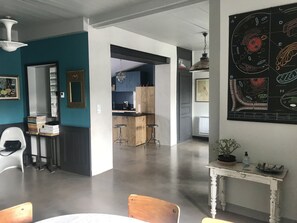 Uma cozinha moderna com banquetas, uma sala de jantar com mesa e cadeiras brancas e uma parede com diagramas científicos.