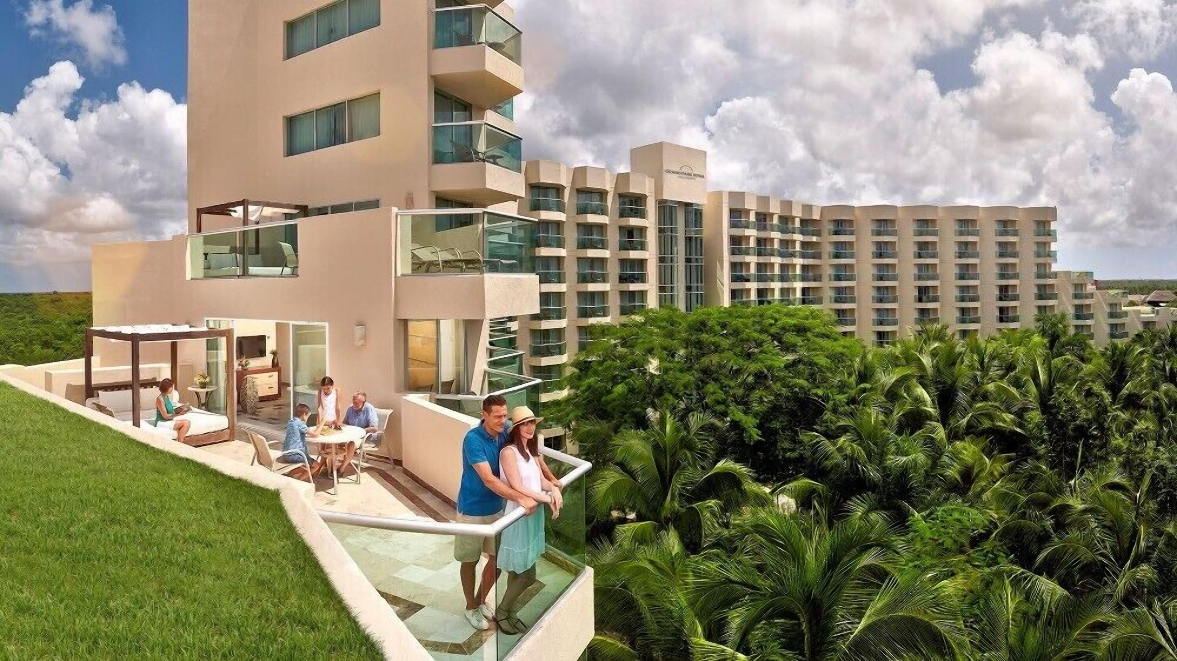 A modern hotel with a glass exterior, a rooftop patio, and lush greenery.