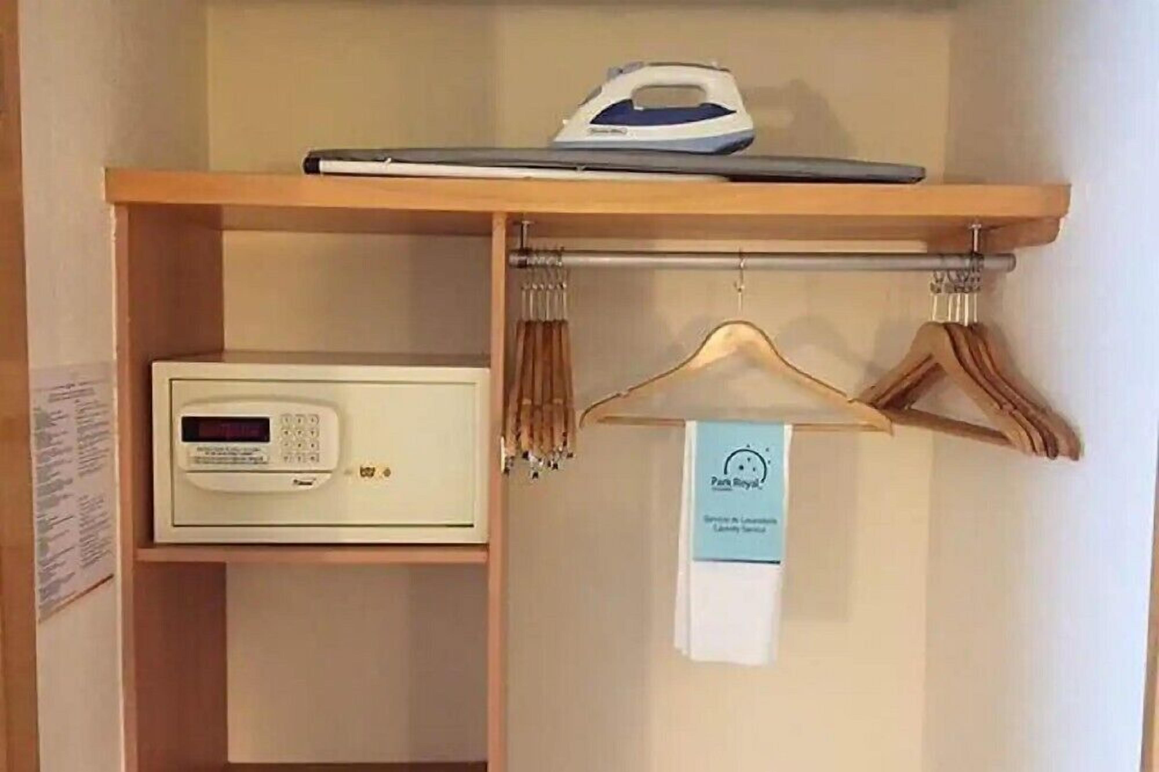 A hotel room with a wooden shelf holding an iron, a digital thermostat, and a hanging garment rack with a towel.