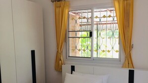 A bedroom with a bed, white bedding, a window with yellow curtains, and a wardrobe. - Thai-scout Home (pran buri)