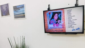 A room with a wooden console table, a wall-mounted TV displaying a poster, and two framed pictures. - Thai-scout Home (pran buri)