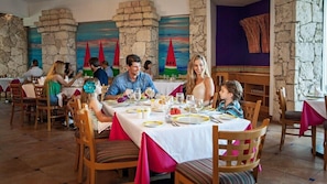A restaurant with stone walls and colorful paintings, wooden chairs, and tables set for dining. - Vibrant Studio with Pools and Hot Tub at Cozumel (San Miguel de Cozumel)