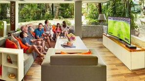 Ein modernes Wohnzimmer mit großem Fernseher, bequemen Sitzmöglichkeiten und Blick auf üppiges Grün.