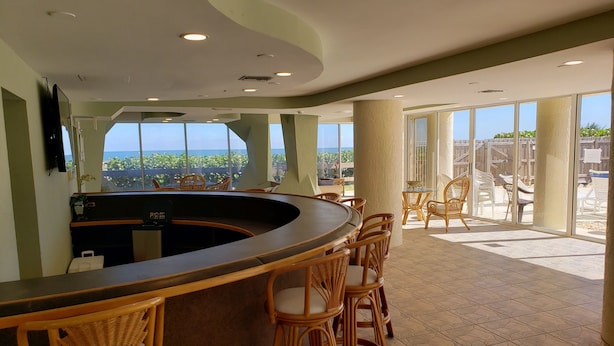 Eine Bar mit Korbstühlen, einer gebogenen Theke und großen Fenstern mit Blick auf das Meer.