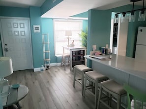 A kitchen with a white refrigerator, a sink, and a window with blinds. There is a ladder leaning against the wall and a table with stools.