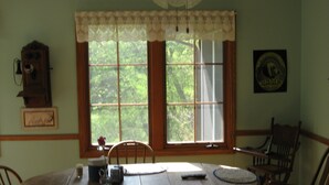 A dining room with a wooden table, four chairs, a clock, and a window with a view of greenery. - 3 Bedroom House in Rural Setting but close to Iowa City/Solon (Solon)