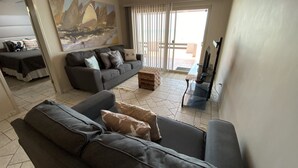 A modern living room with a grey sofa, a coffee table, and a painting on the wall. - Shell Yeah! 🐚 🏝 Paradise 🦀 (Son)