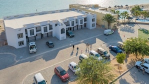 A modern building with a flat roof, multiple parking spaces, and a pool area with umbrellas. - Shell Yeah! 🐚 🏝 Paradise 🦀 (Son)