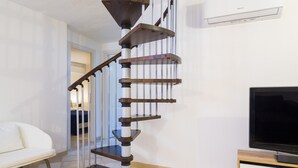 Un intérieur moderne avec un escalier en colimaçon, un téléviseur à écran plat et un canapé blanc.