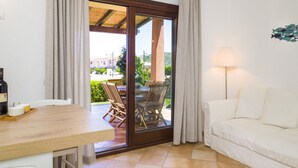 Une pièce comprenant une table à manger, un canapé et une porte-fenêtre coulissante donnant sur une terrasse extérieure avec une table et des chaises.