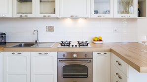 Une cuisine moderne avec des meubles blancs, une hotte en acier inoxydable, un four encastré et une cuisinière à gaz.