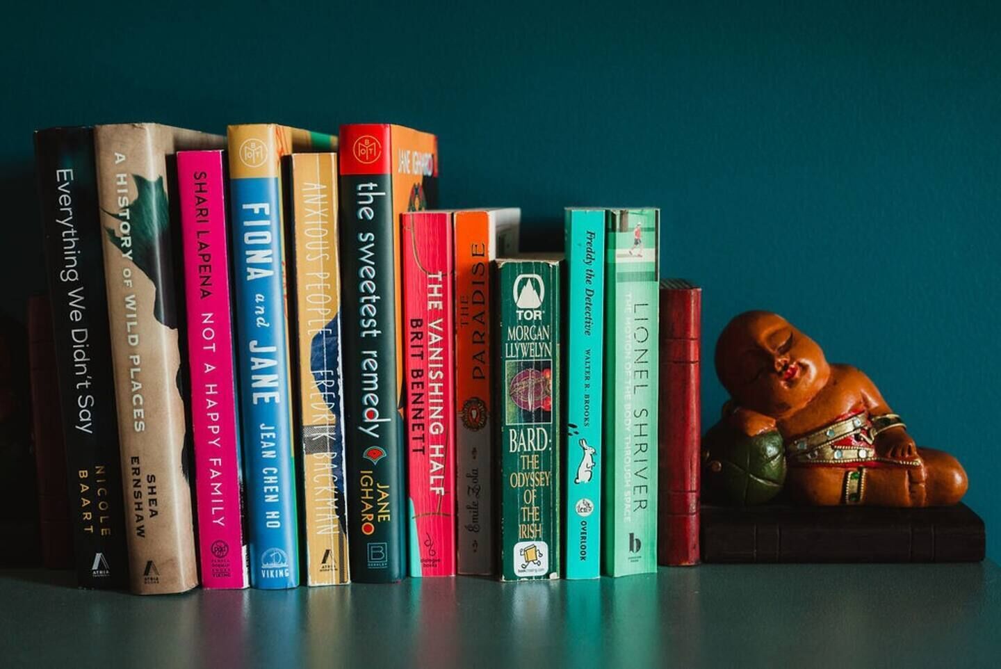 A collection of books on a shelf with a small figurine to the right.