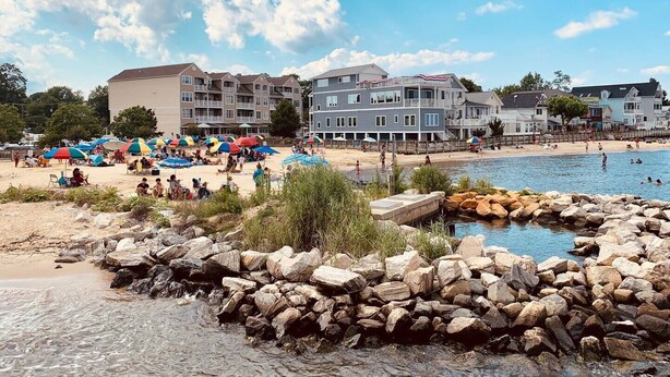 Ein Strand mit felsigem Ufer, einem Badebereich und mehrstöckigen Gebäuden im Hintergrund.