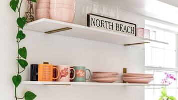 A shelf with pink and white dishes, a sign reading "NORTH BEACH," and a plant with heart-shaped leaves.