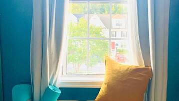 Una habitación con un banco de madera, un cojín amarillo, una cesta de mimbre y una ventana con cortinas.