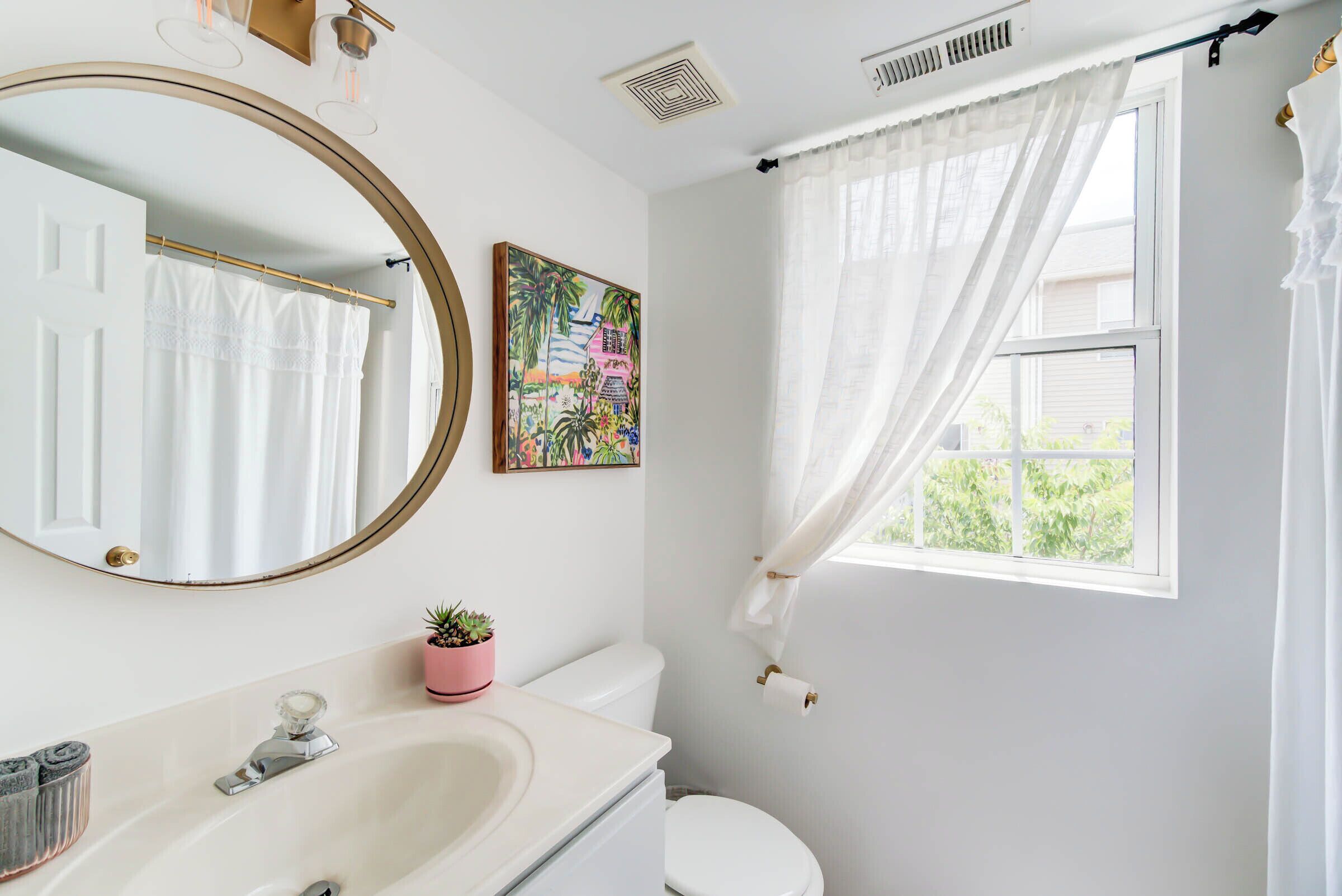 Un baño con un lavamanos blanco, un espejo, un inodoro y una ventana con cortina.