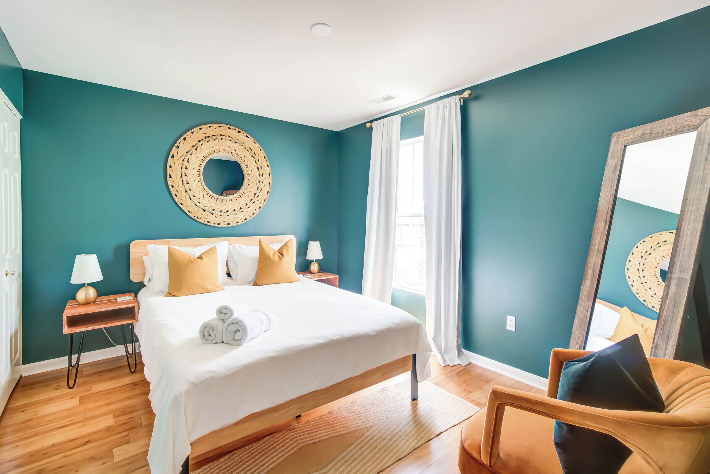 A bedroom with a bed, two bedside tables, a mirror, and a window with curtains.