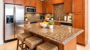 Une cuisine dotée de meubles en bois, d’appareils électroménagers en acier inoxydable, d’un plan de travail en granit et d’un îlot central avec des tabourets.