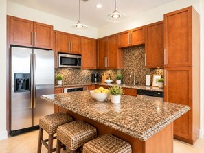 Cozinha com armários de madeira, eletrodomésticos de aço inoxidável, bancada de granito e uma ilha central com banquetas.