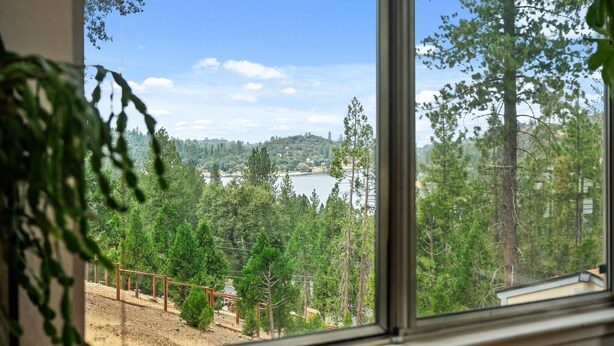 A view from a window overlooking a forested area with a lake and distant hills. - Big Oso Cabin: Views, Private Hot Tub & Backyard Putting Green (Groveland)
