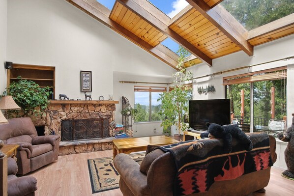 A cozy living room with a stone fireplace, wooden ceiling beams, and a large TV.